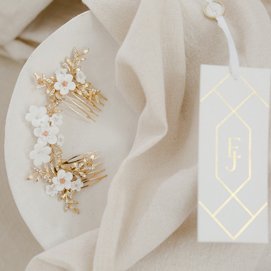 Gold hair accessories with white flowers on a white plate, next to a branded tag.