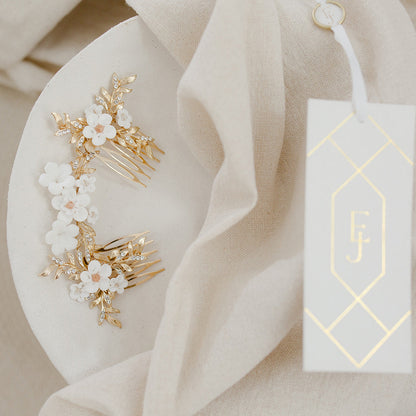 Gold hair accessories with white flowers on a white plate, next to a branded tag.