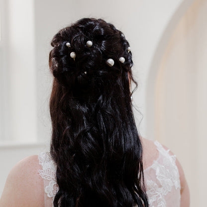 Bride with long, wavy hair adorned with pearls, wearing a white lace dress.