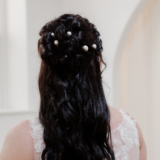Bride with long, wavy hair adorned with pearls, wearing a white lace dress.