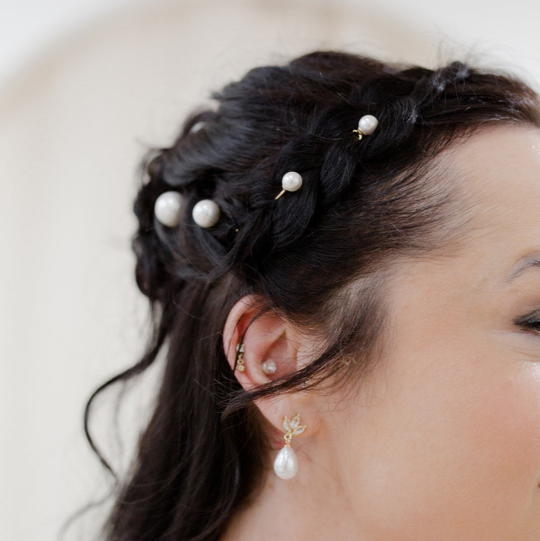 Close-up of a person with braided hair adorned with pearl hairpins, wearing matching earrings.