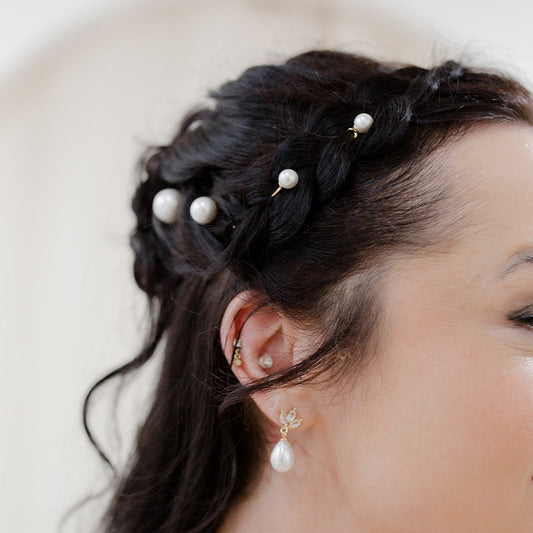 Close-up of a person with braided hair adorned with pearl hairpins, wearing matching earrings.